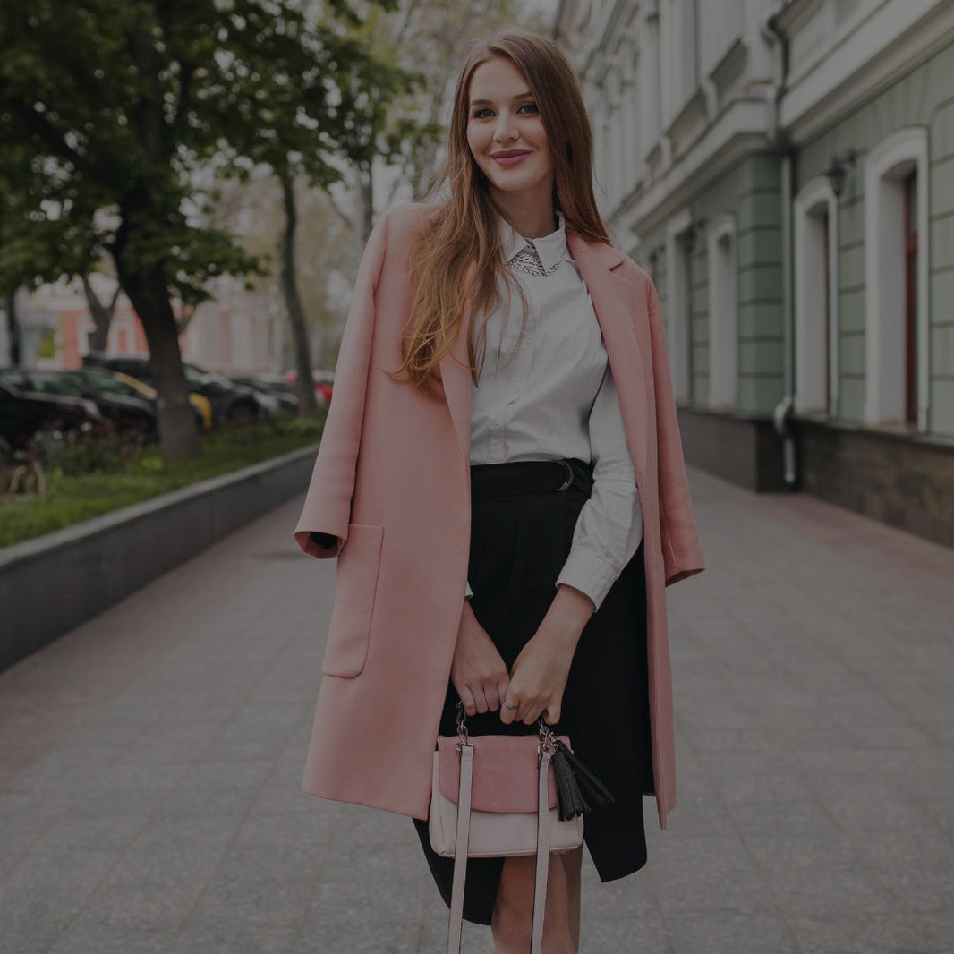Woman in a pink coat holding a matching handbag on a city street.