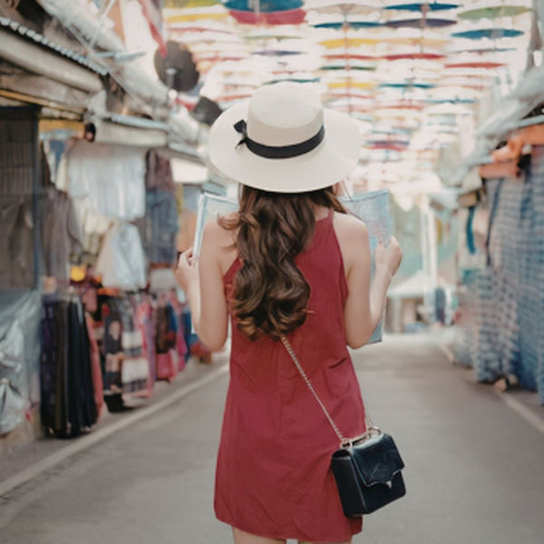 Woman in a red dress and white hat exploring a colorful market street.