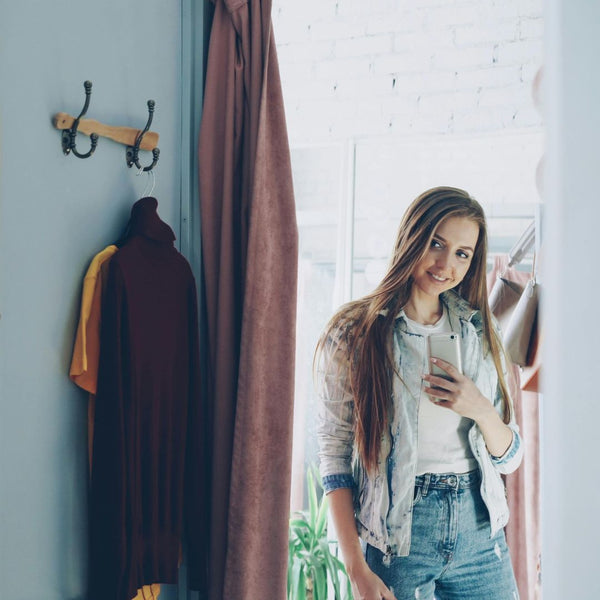 Woman standing in a room with clothes hanging on hooks and a plant in the corner.
